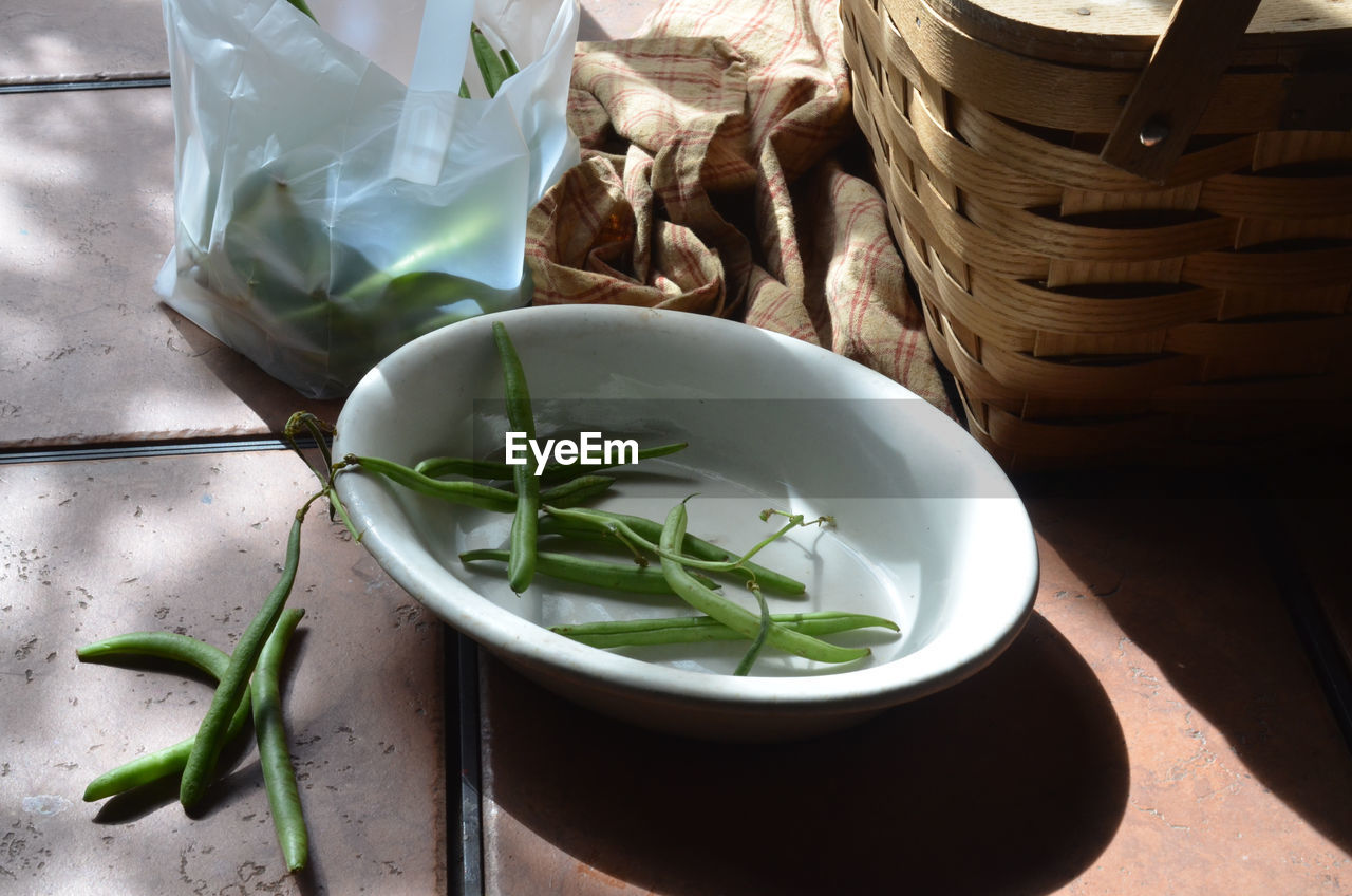High angle view of green beans by wicker basket on table