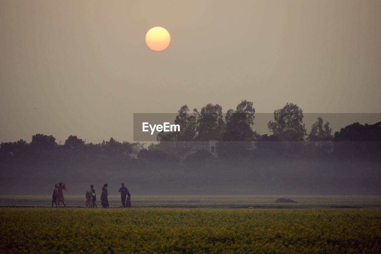 People on field against clear sky during sunset