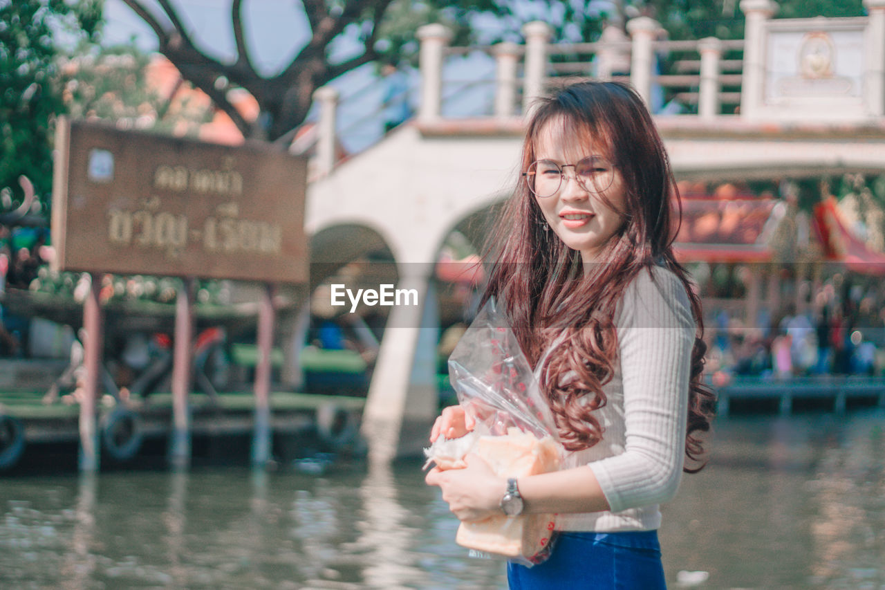 Portrait of young woman standing against river and text on board