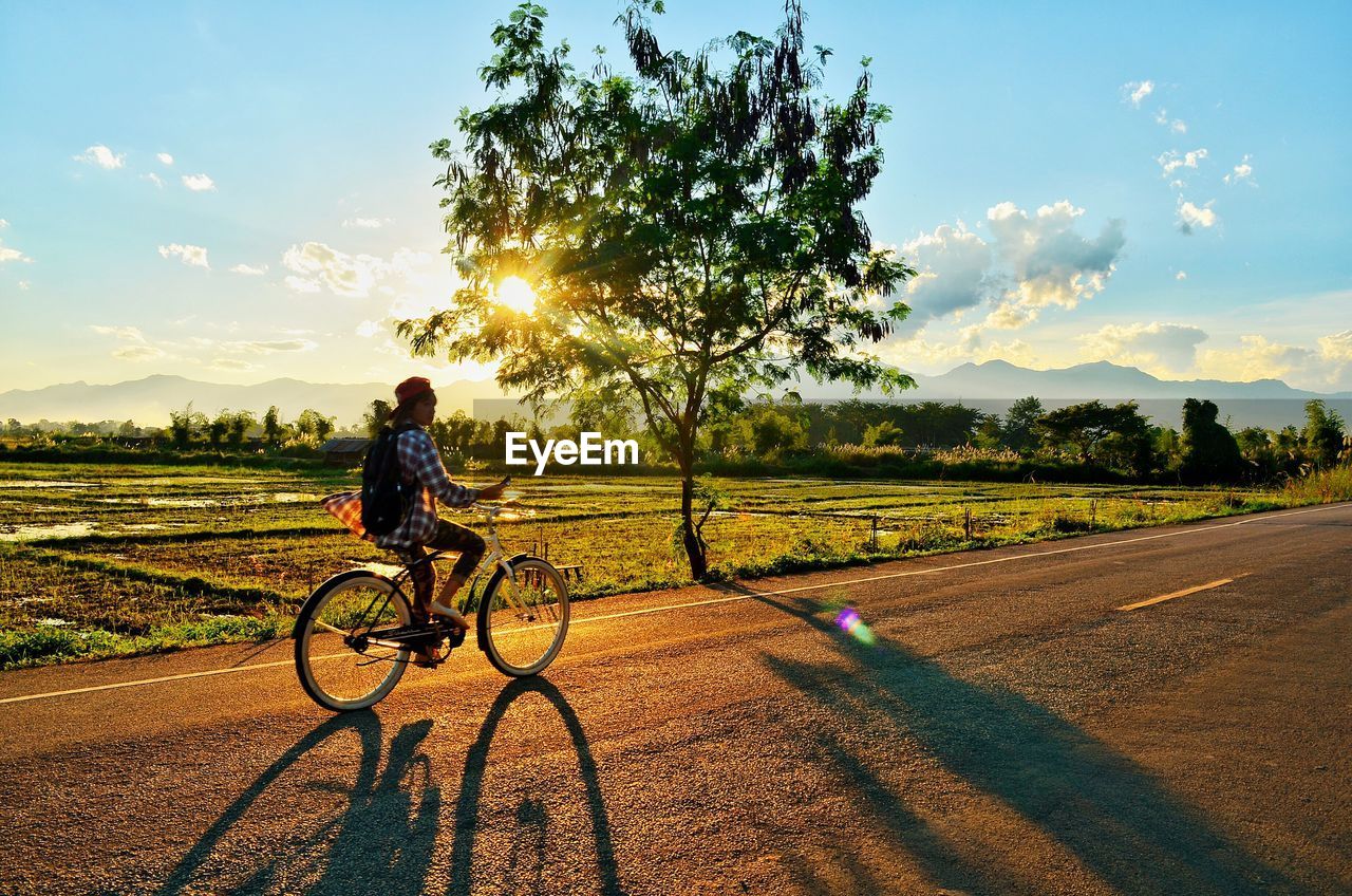 MAN RIDING BICYCLE ON FIELD AGAINST SKY