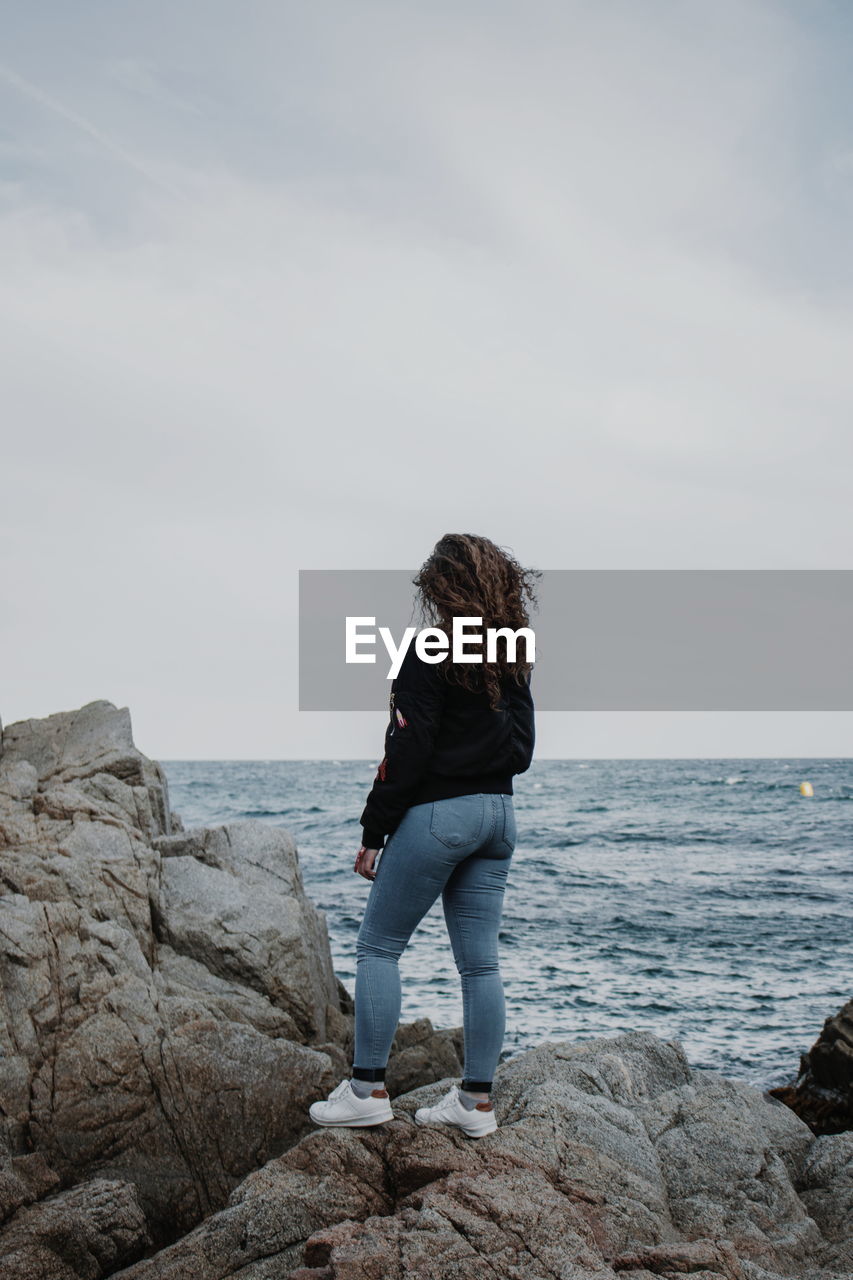 Rear view of woman standing on rock against sky