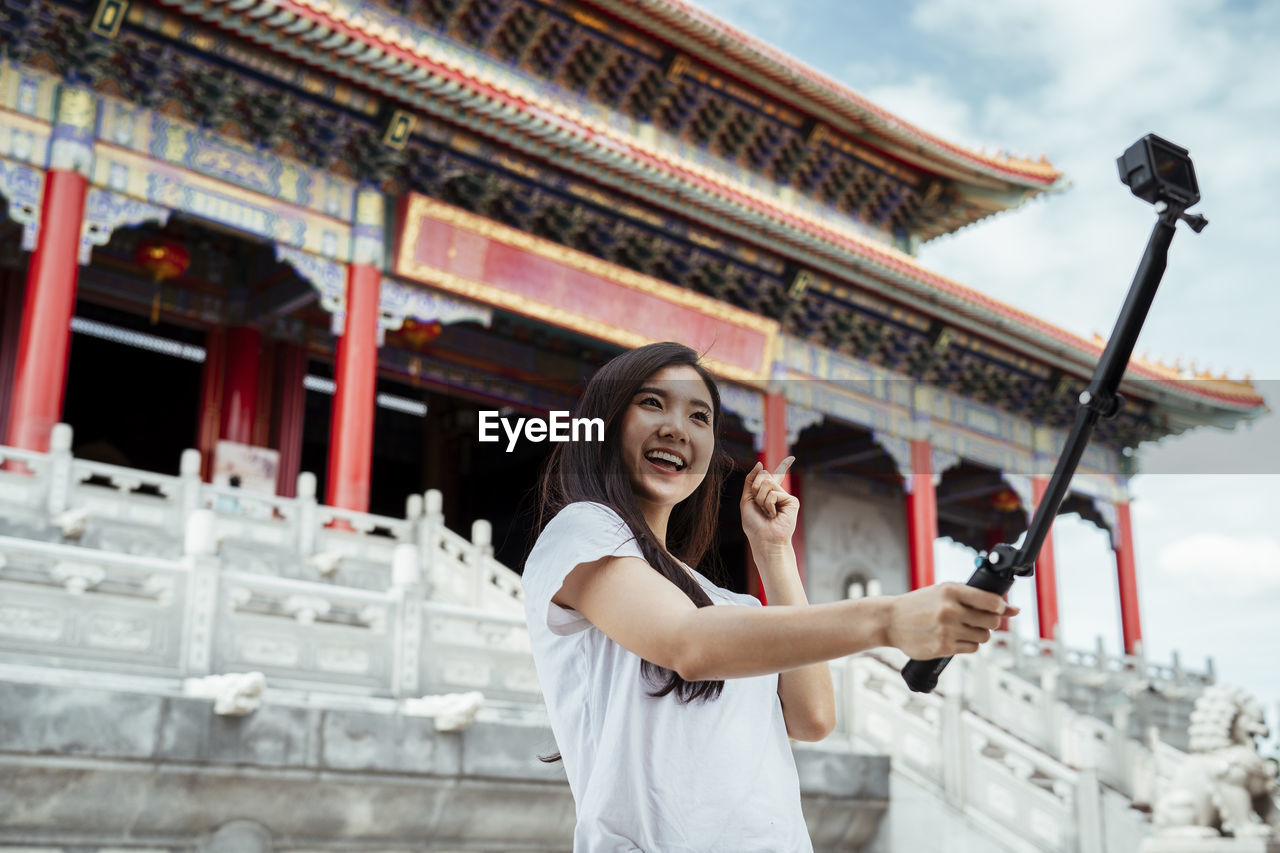 Smiling woman vlogging while standing against temple