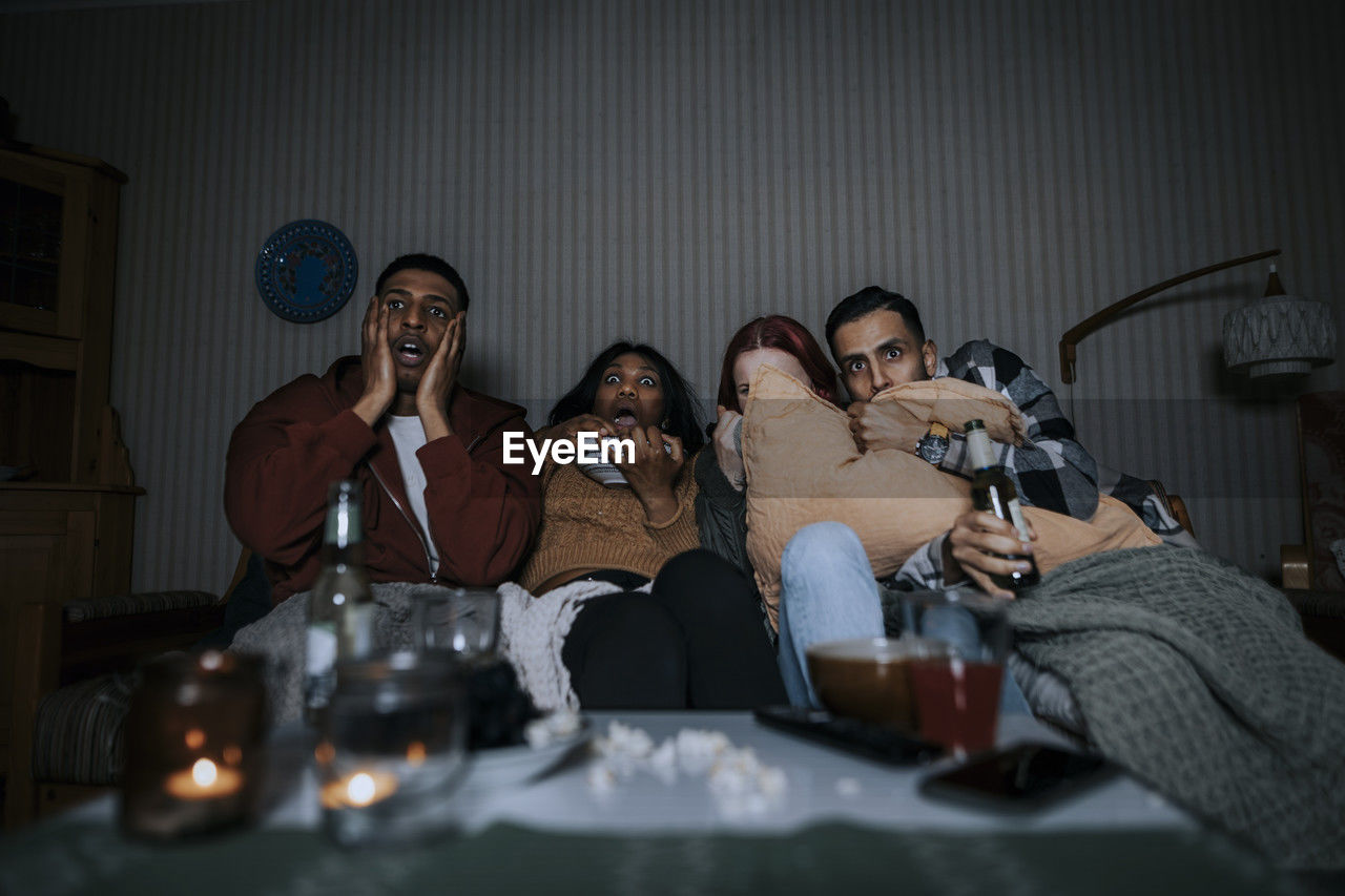 Frightened multiracial friends watching scary movie in cabin