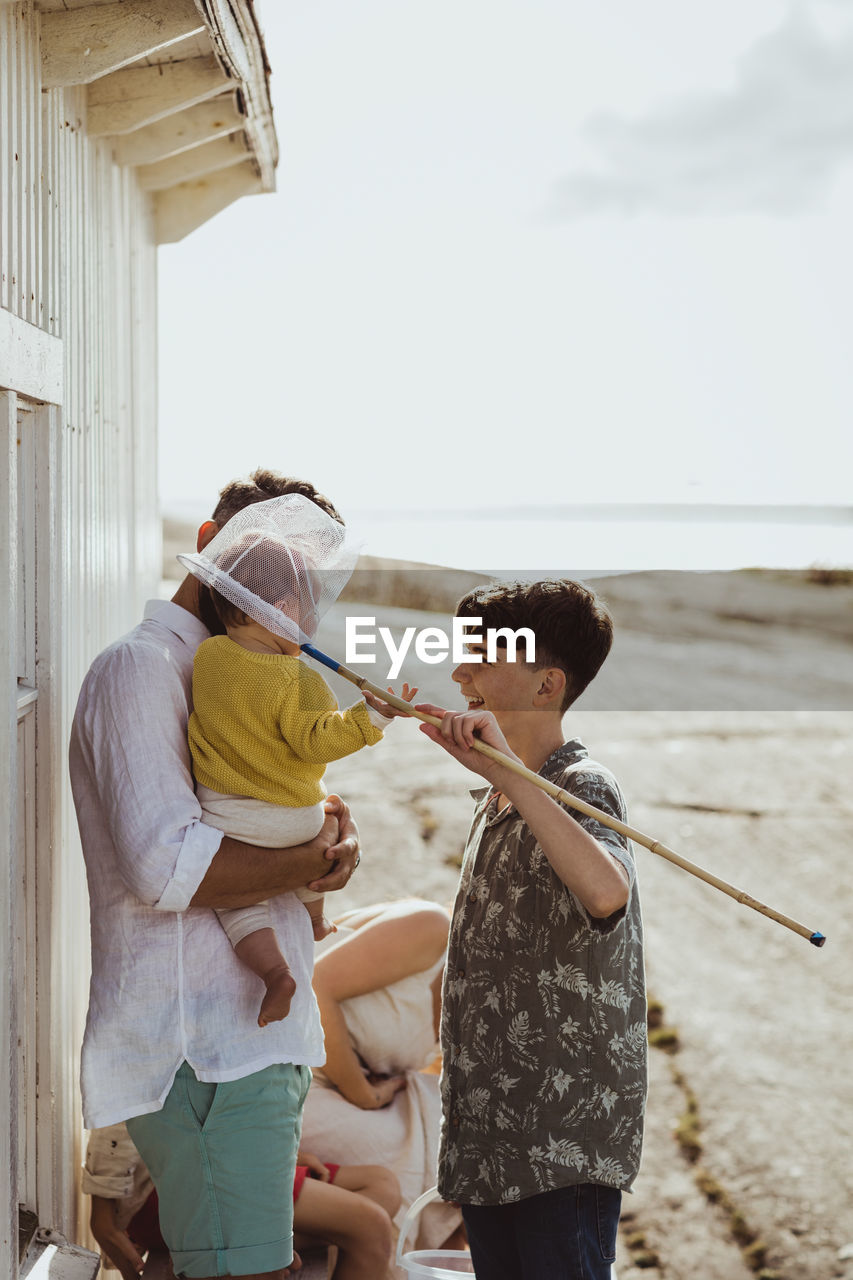 Side view of playful brother covering sister's head with fishing net by cabin