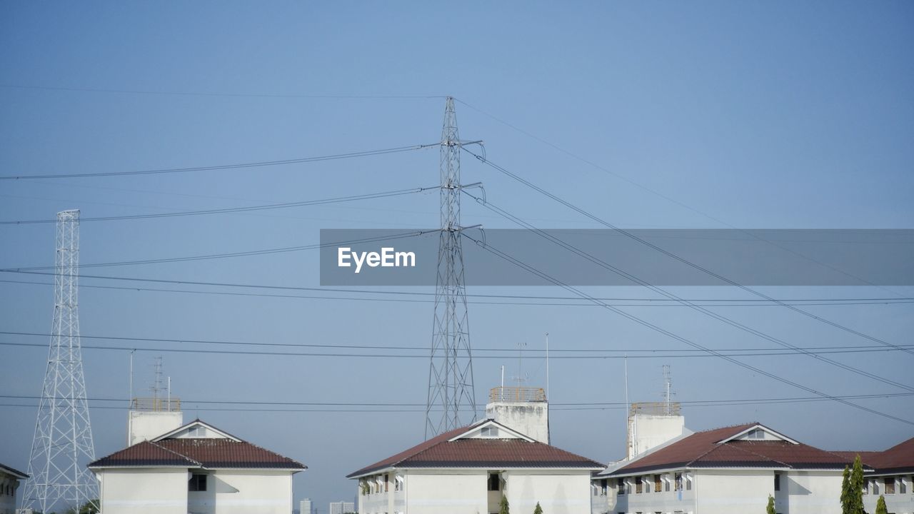 Low angle view of electricity pylon and buildings against clear sky