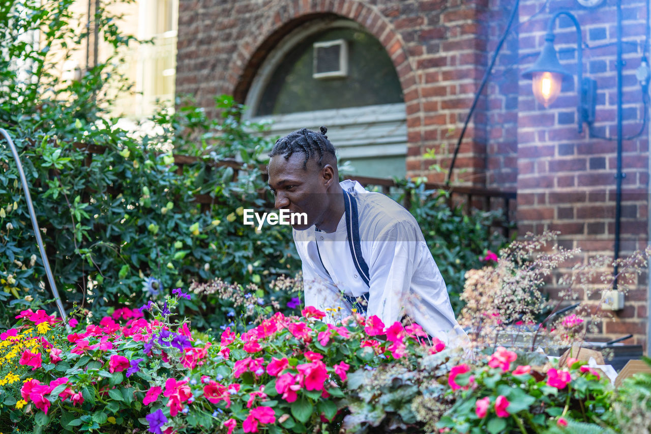 REAR VIEW OF MAN WORKING AT FLOWERING PLANTS