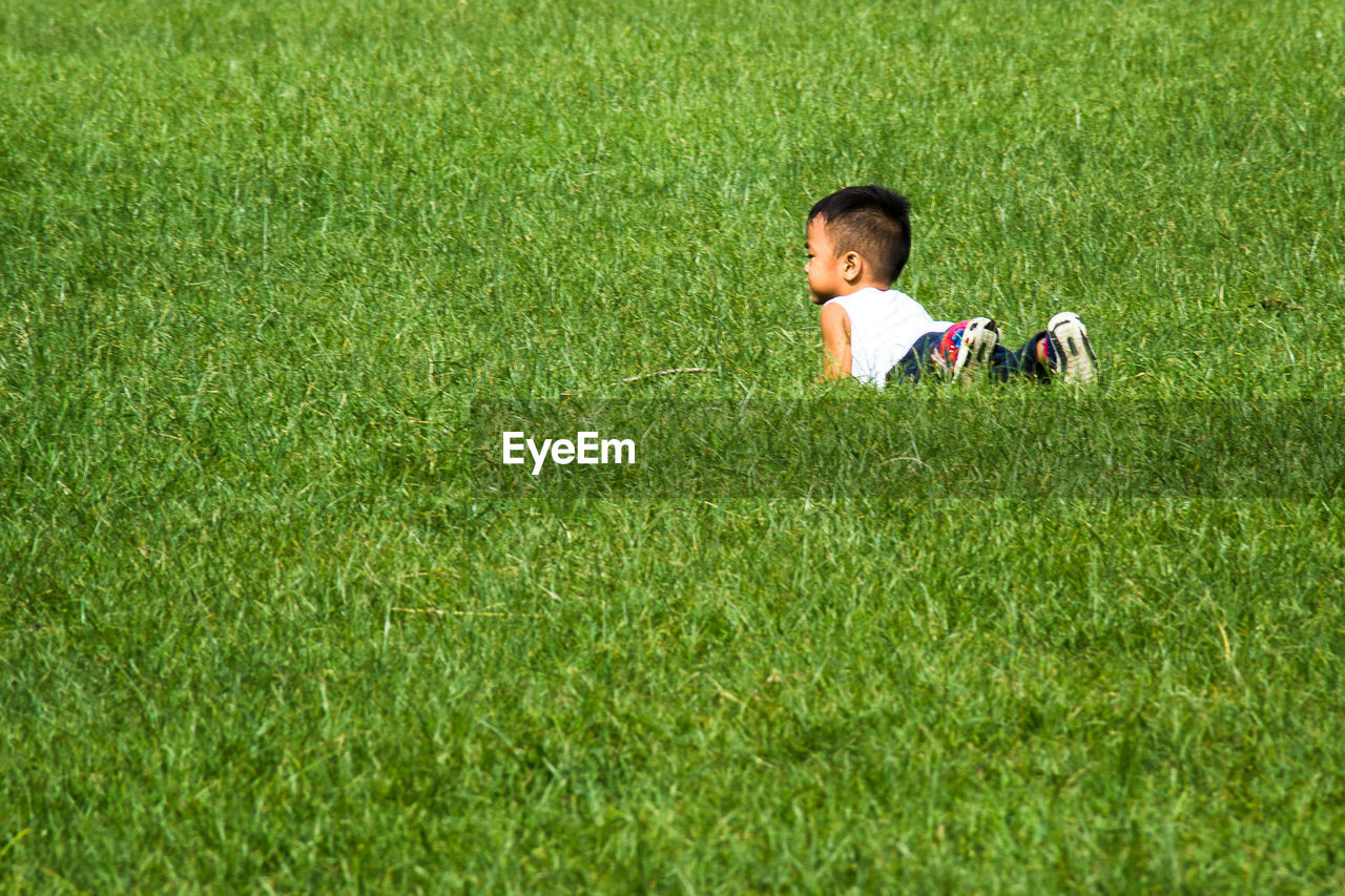 REAR VIEW OF GIRL PLAYING ON GRASSY FIELD
