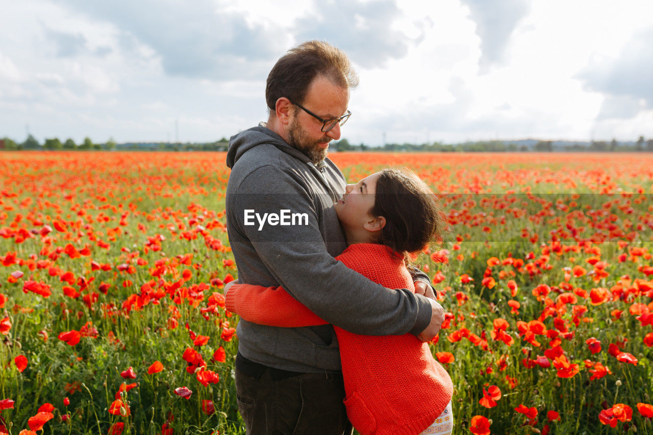 Father and daughter hugging each other on a sunny day in the big field of poppies