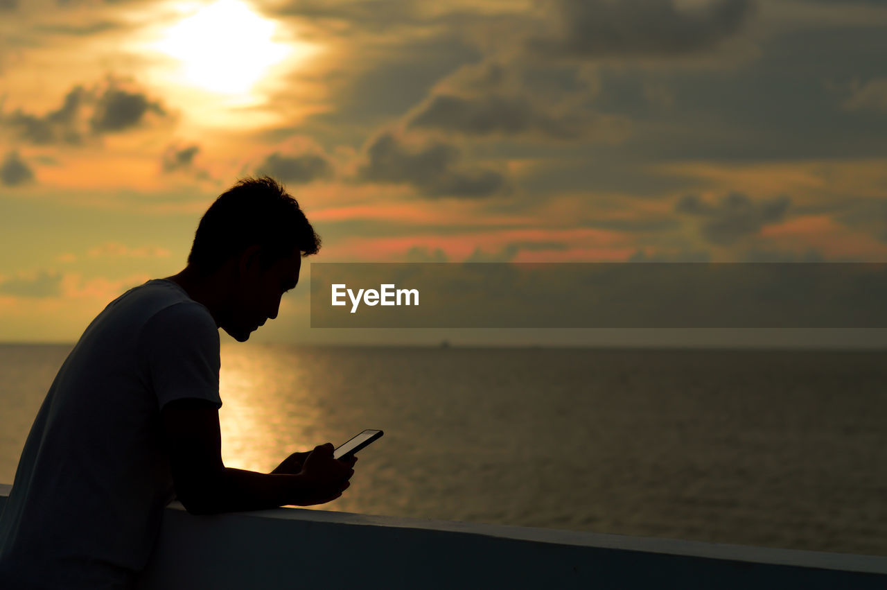 Man using phone by sea during sunset