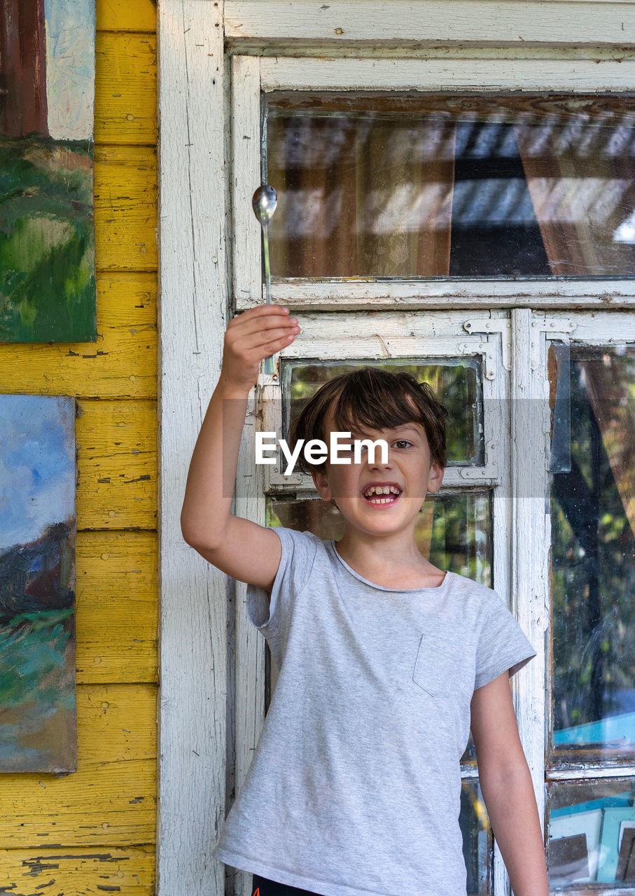 Portrait of emotional boy standing outdoors, holding spoon in hand