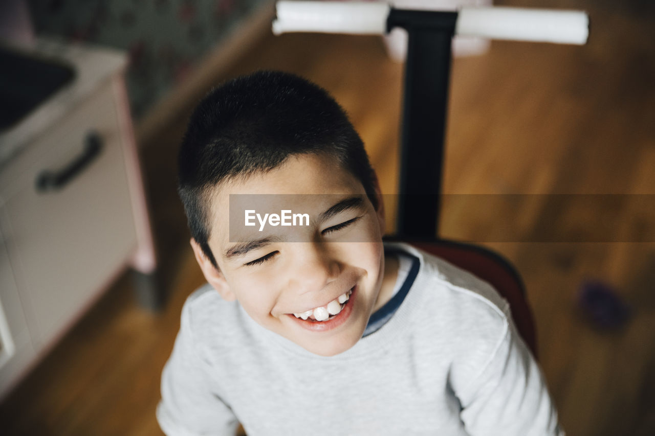 High angle view of happy disabled boy looking away while sitting on wheelchair at home