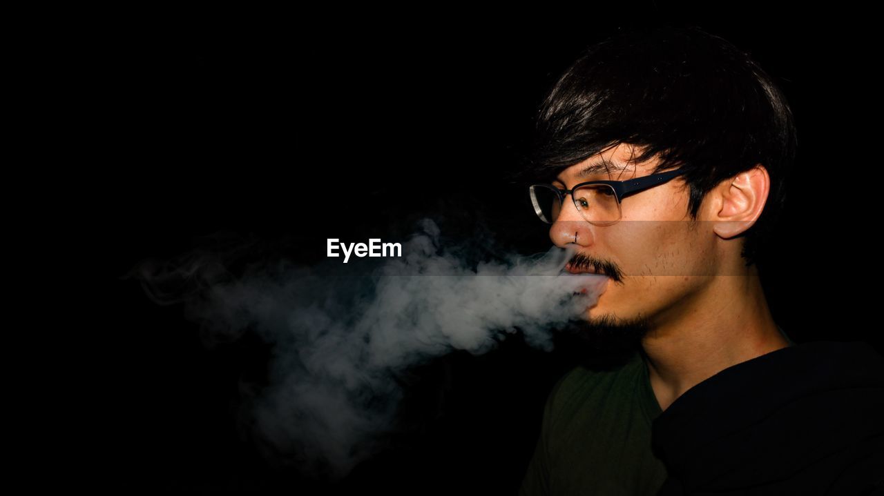 Portrait of young man smoking over black background