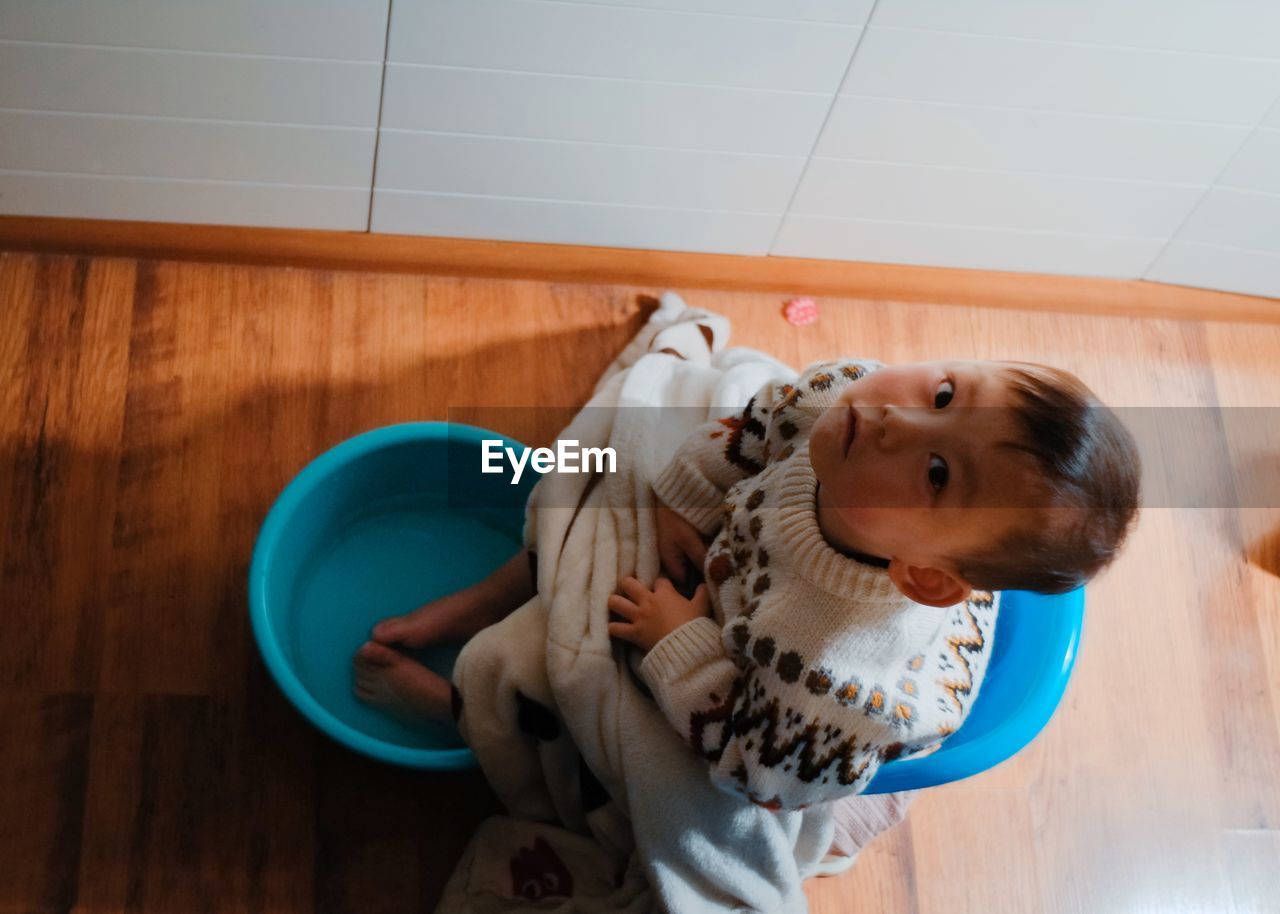 High angle view of cute baby boy with feet in bucket sitting at home