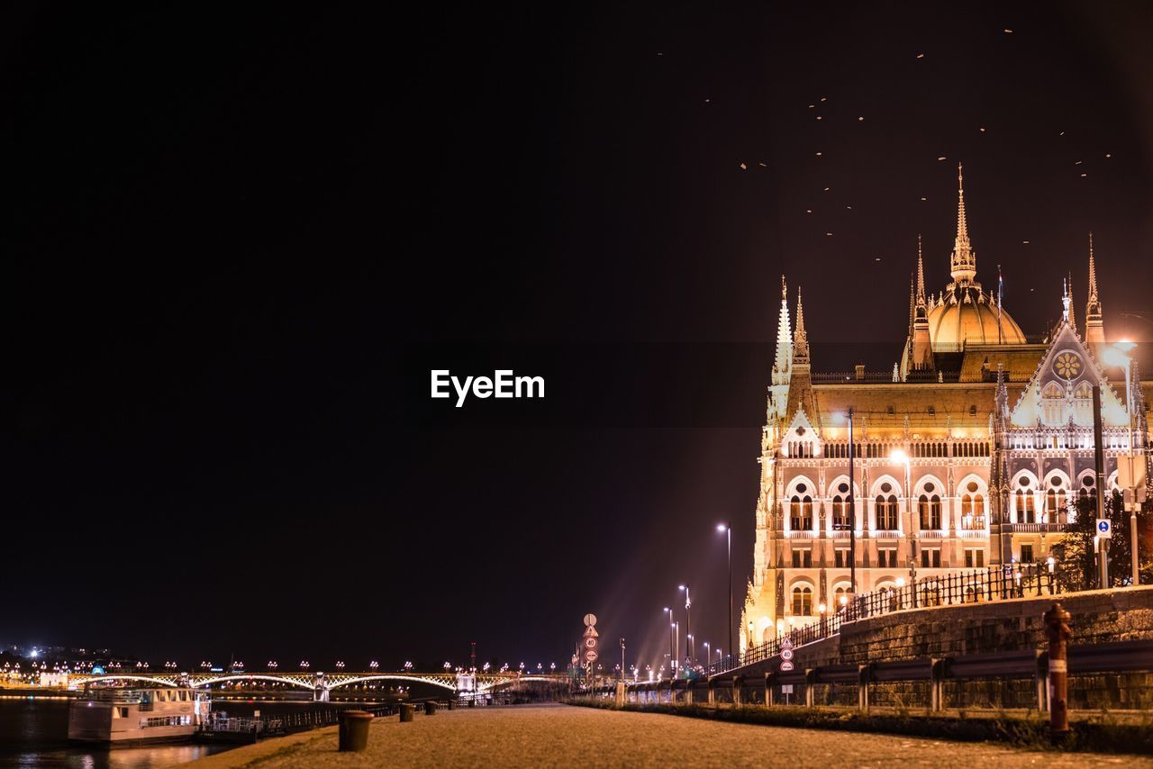 Hungarian parliament building by road against sky in city at night