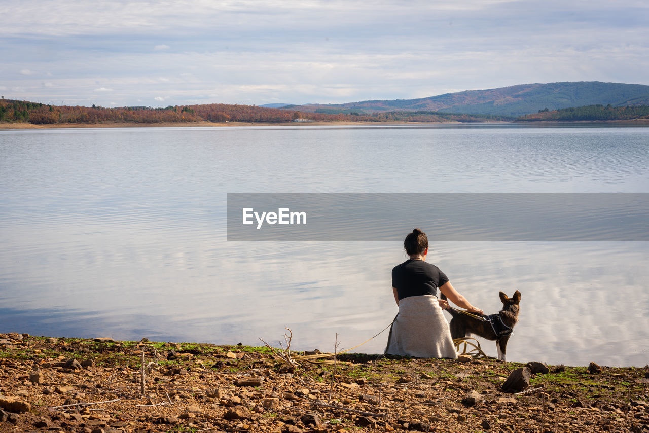 Rear view of woman with dog by lake against sky