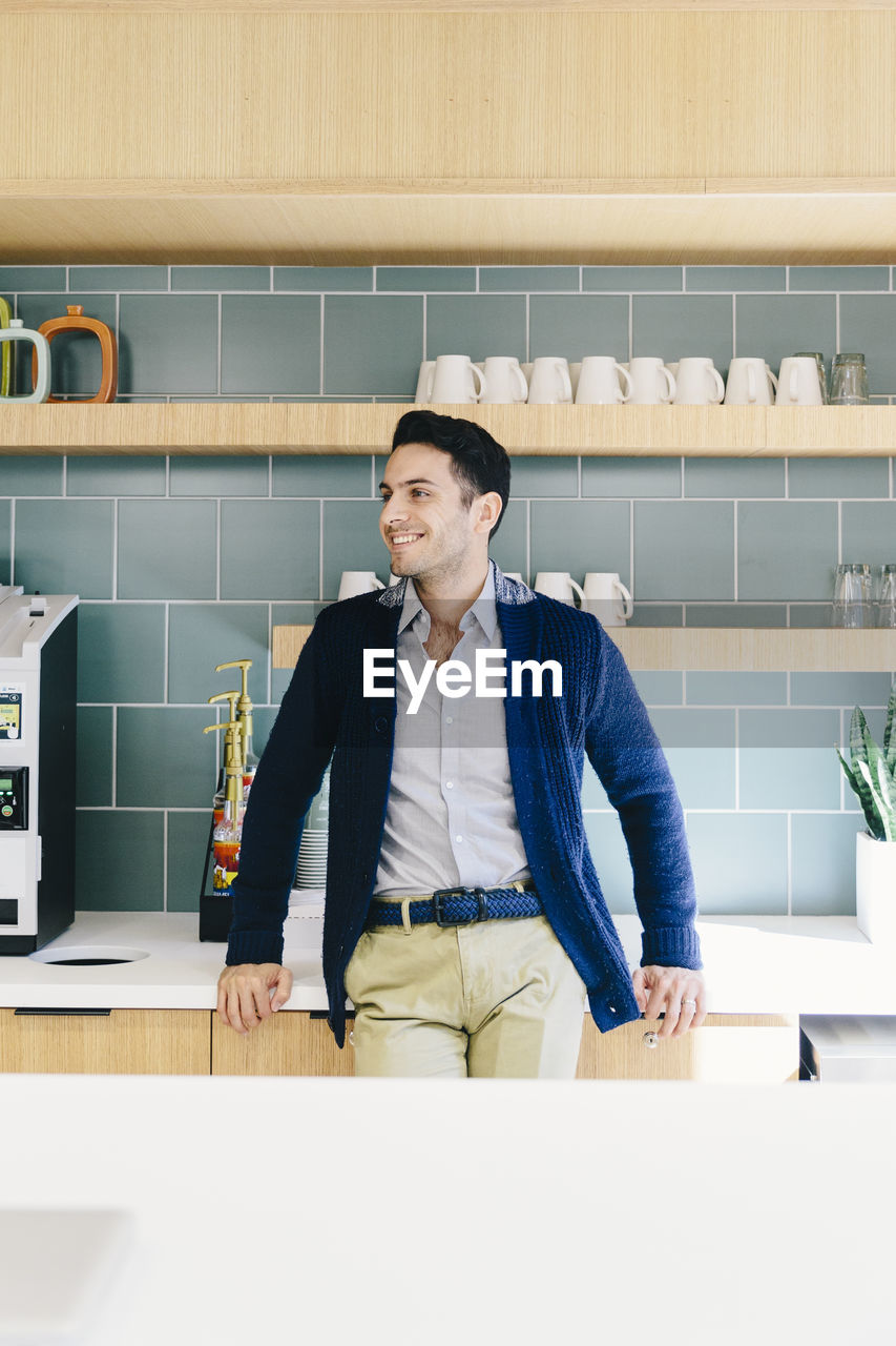 Businessman looking away while standing by kitchen counter in cafeteria at creative office