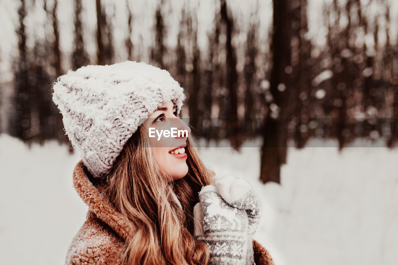 Woman standing on the white snow in winter forest. girl is smiling and happy with closed eyes