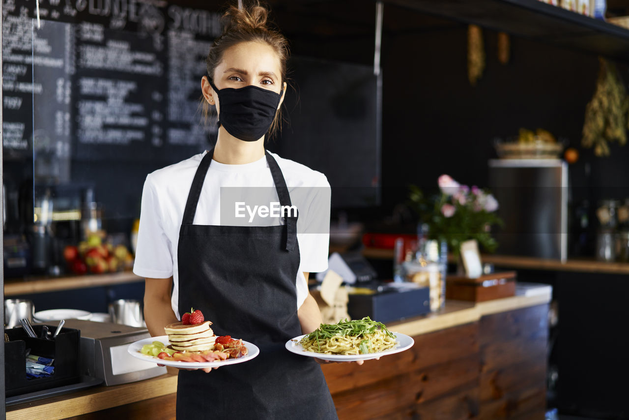 Portrait of barista wearing protective mask while serving food in coffee shop