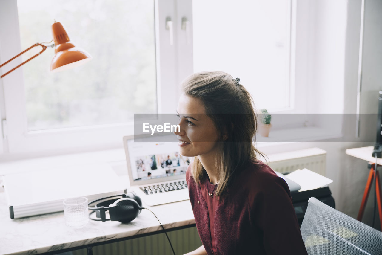 Confident businesswoman looking away while sitting at desk in office