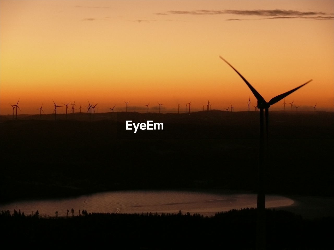 Silhouette wind turbines on field against sky during sunrise