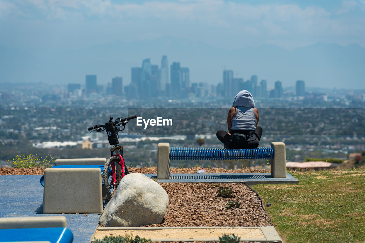 Woman sits on bench and looks at la city scape after a long bike ride