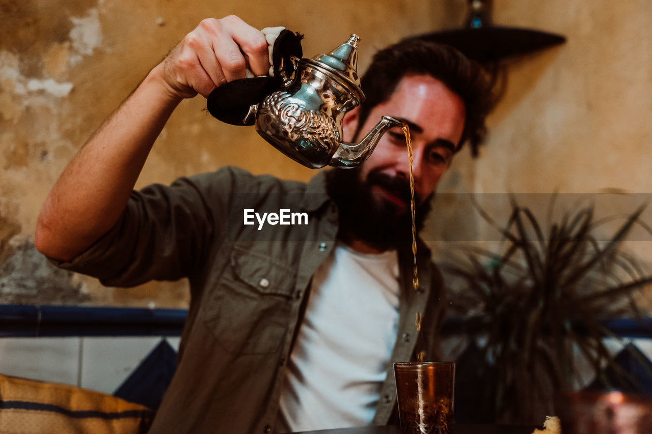 Man pouring drink in glass on table while sitting in restaurant