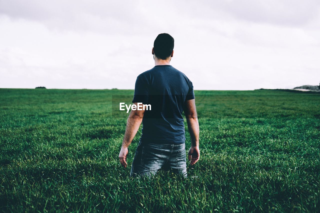 Rear view of man standing in field against sky