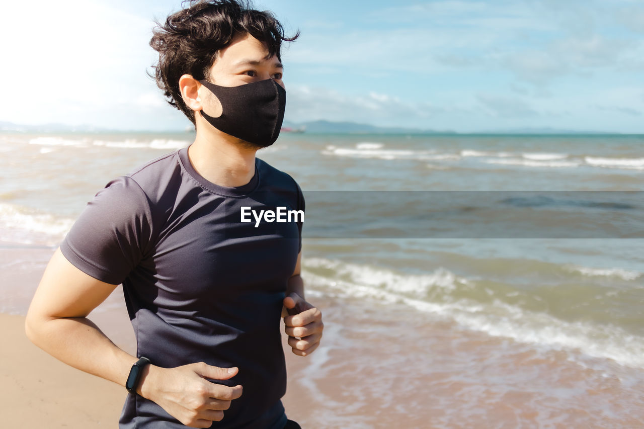 Young man standing on beach against sky