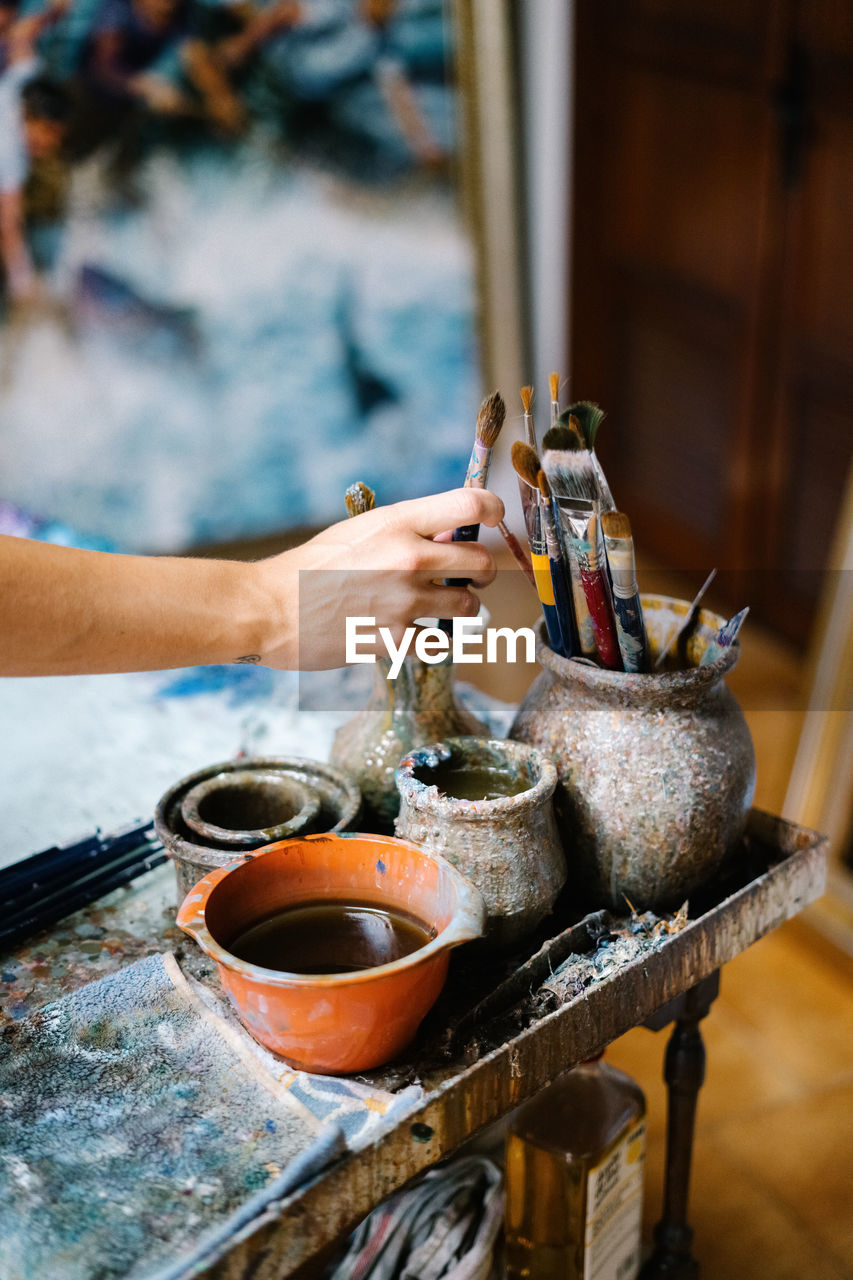 Anonymous female artist taking paintbrush from pot with various brushes in art workshop