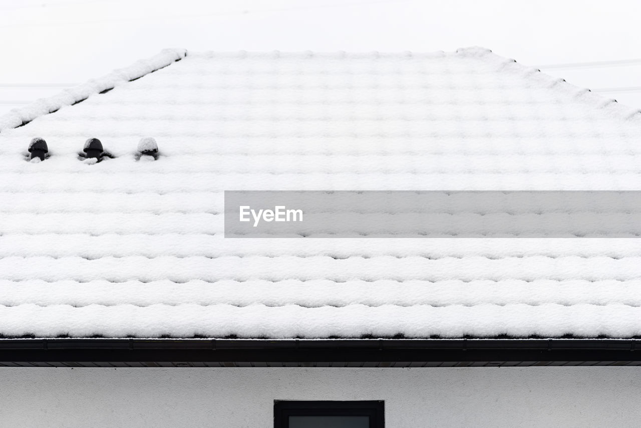 The roof of a single-family house is covered with snow against a cloudy sky,