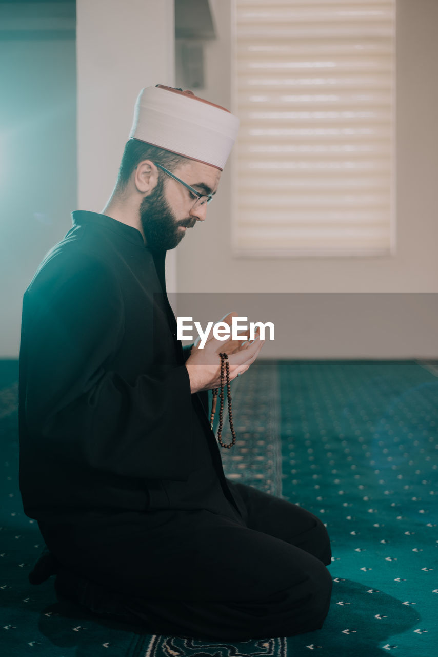 Side view of man praying while sitting in mosque