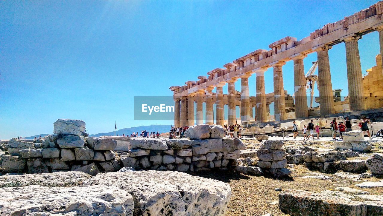 People at ruined historic colonnade against blue sky