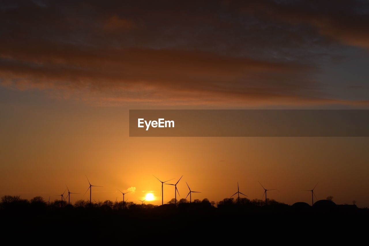 SILHOUETTE WIND TURBINES ON LAND AGAINST SKY AT SUNSET
