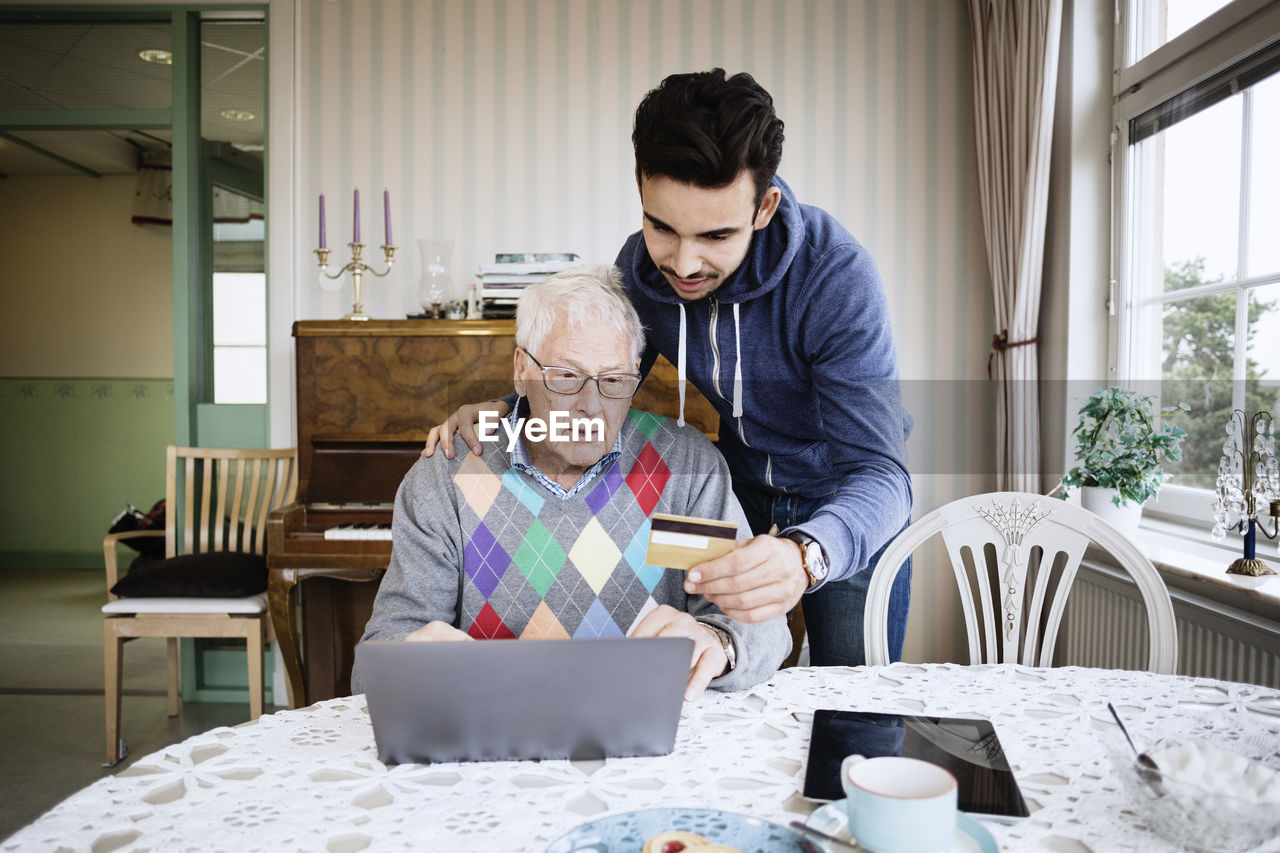 Caretaker and senior man using credit card to shop online