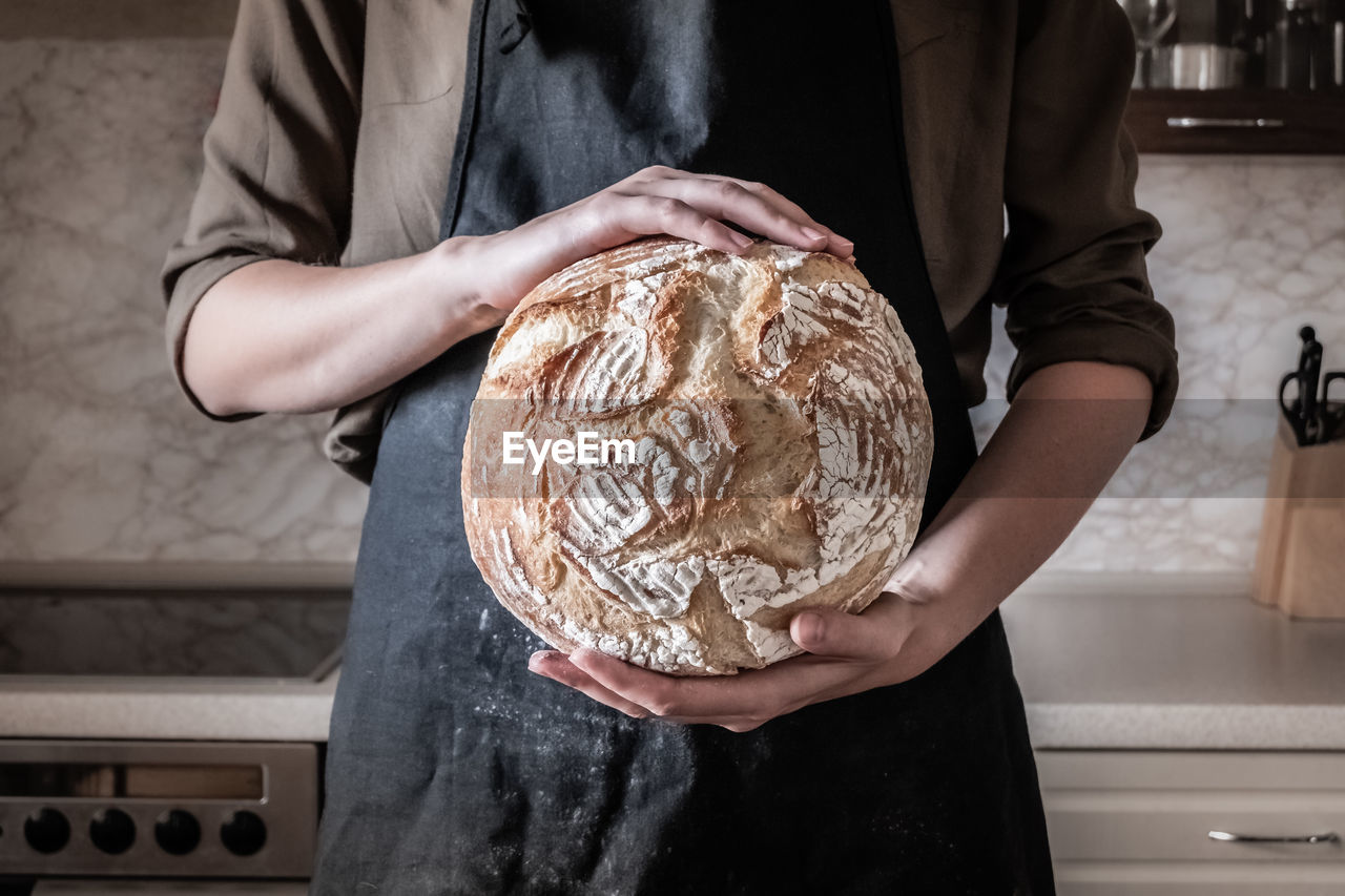 Midsection of baker holding baked bread in bakery