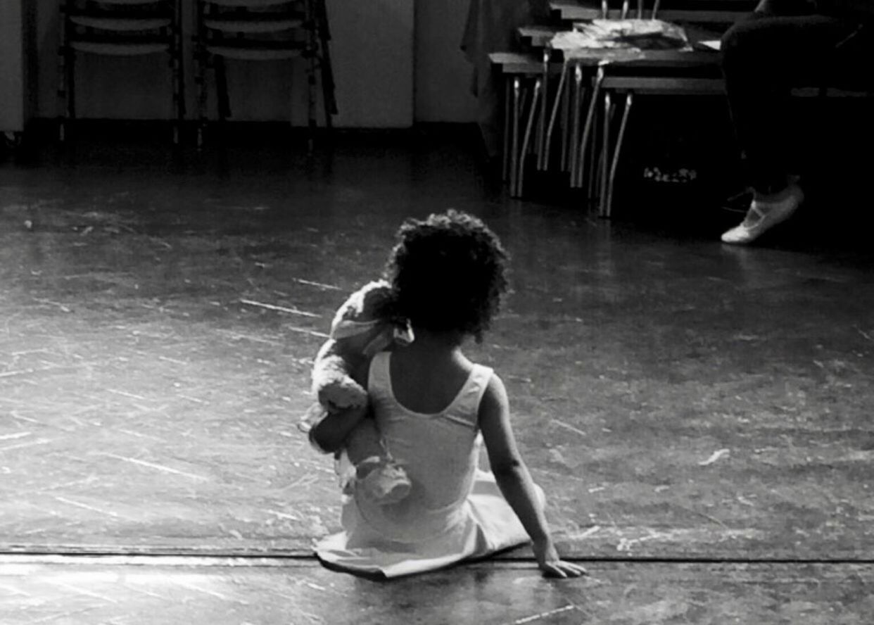 Rear view of girl with teddy bear sitting on floor at ballet studio