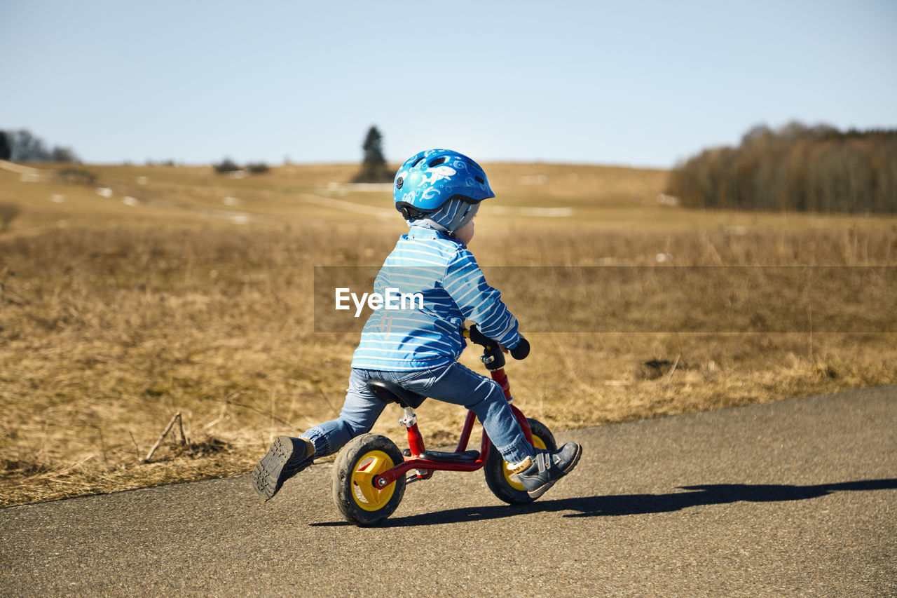 Boy with cycling helmet riding balance bicycle on road