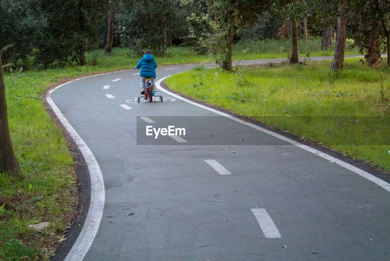 Rear view of boy riding bicycle on road
