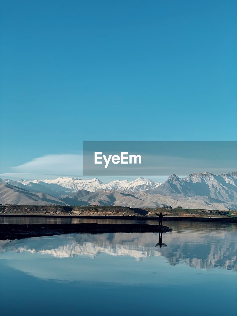 Scenic view of lake and snowcapped mountains against blue sky