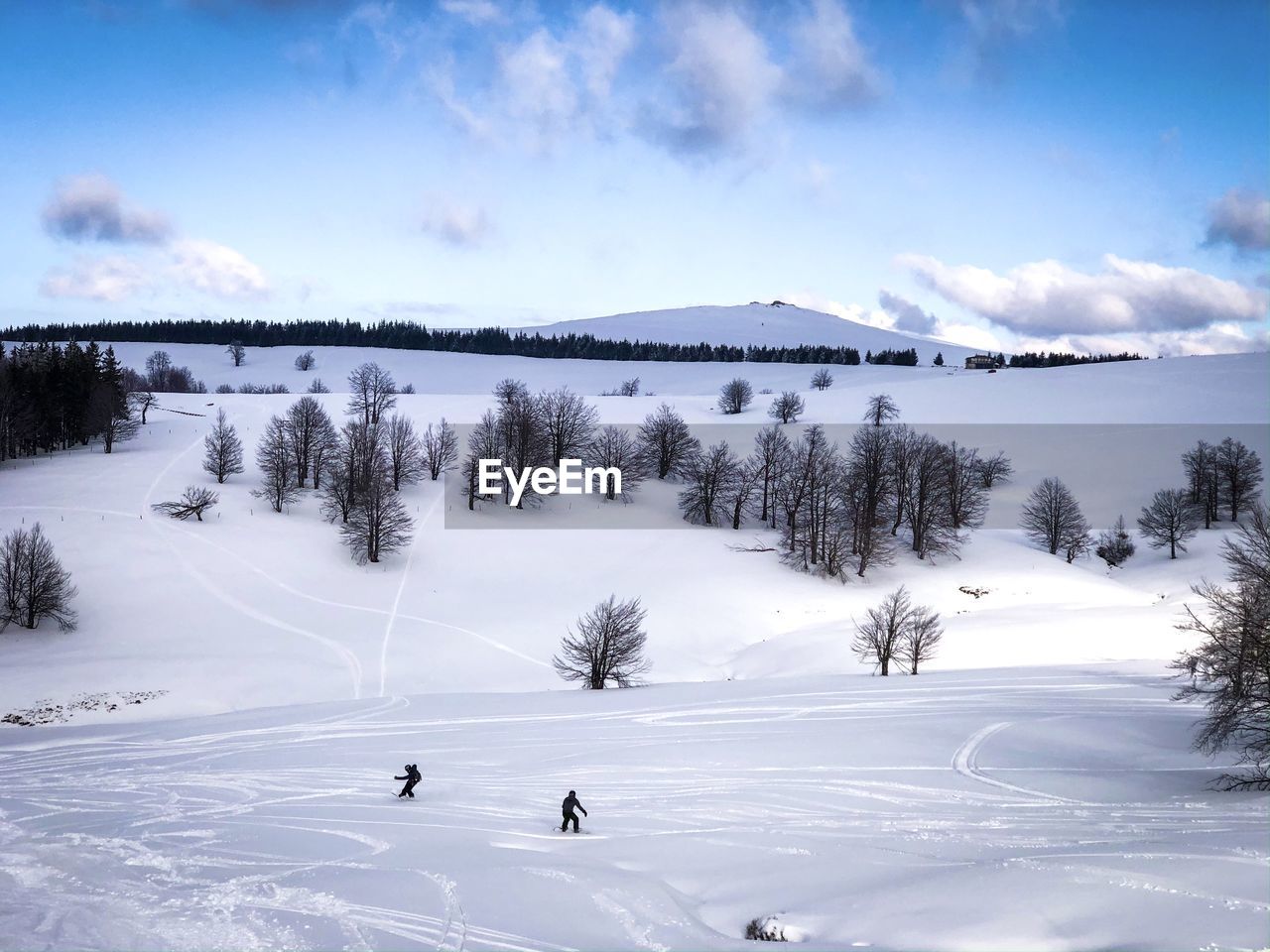 Scenic view of snowcapped mountain against sky and snowboarders on the slope