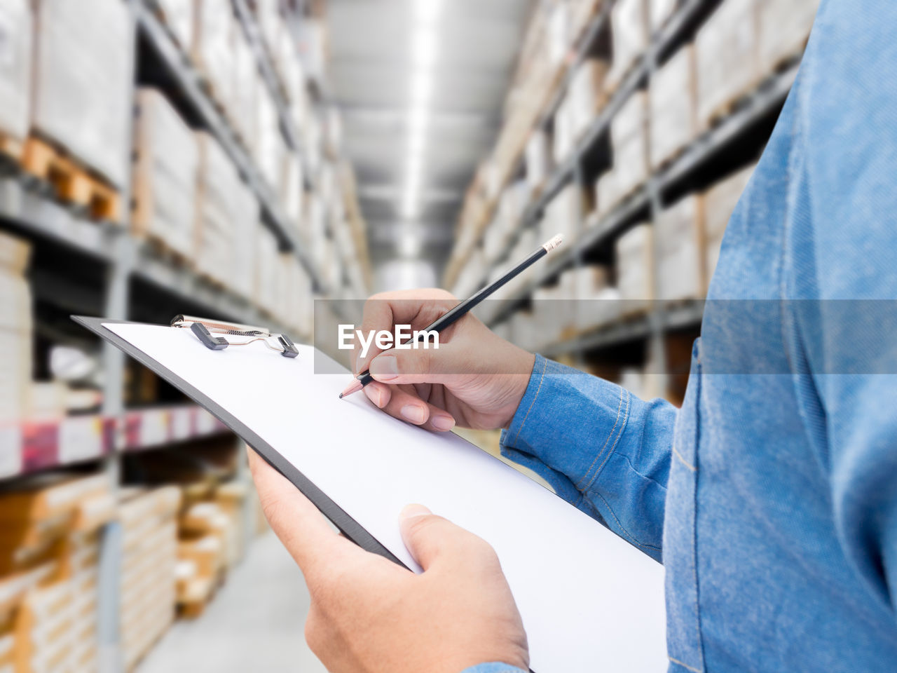 Midsection of man writing in checklist by shelves