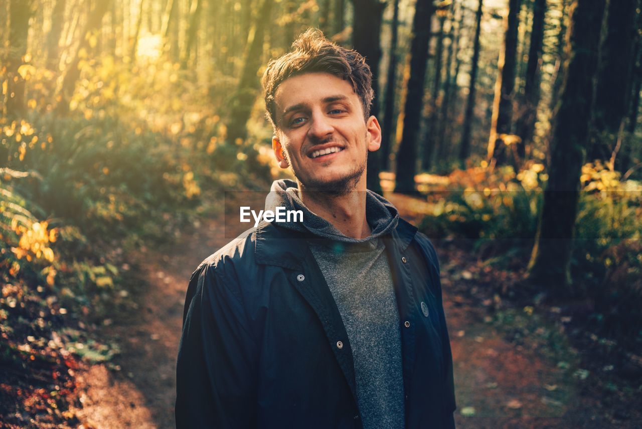 PORTRAIT OF SMILING YOUNG MAN STANDING IN FOREST