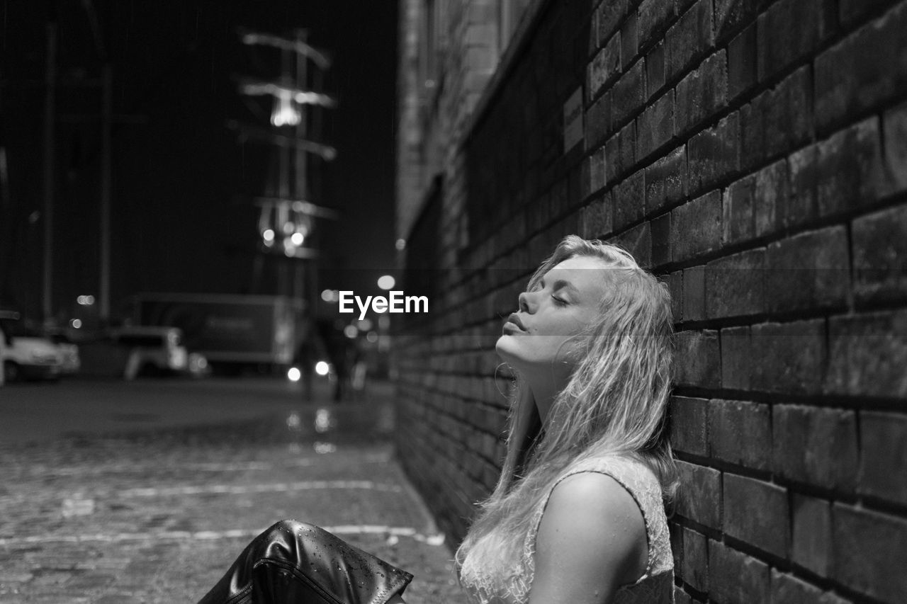 Close-up of young woman leaning against brick wall