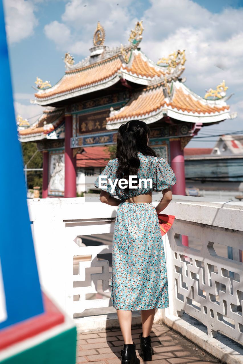 Portrait of woman in blue modern cheongsam holding a red fan at chinese temple 