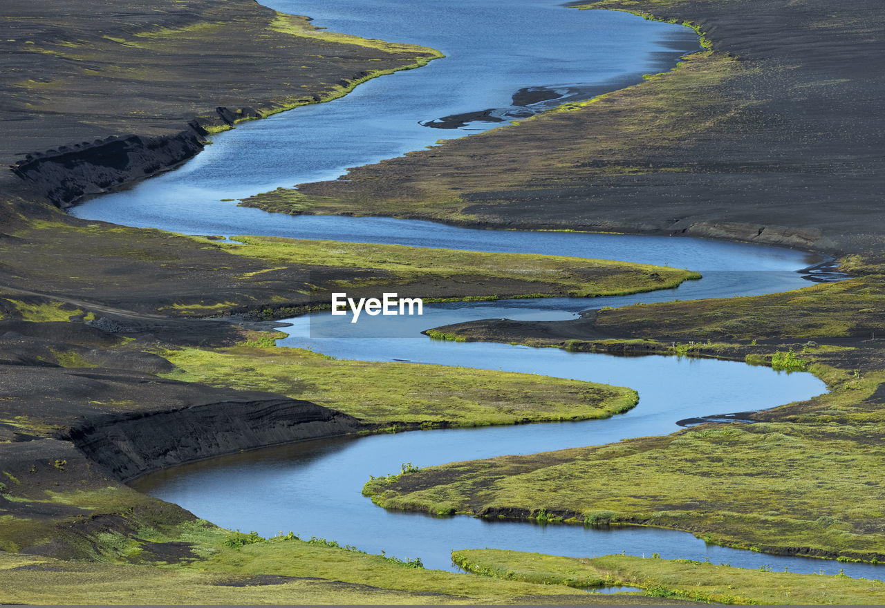 From above of picturesque landscape of bright blue river flowing among volcanic terrain in iceland