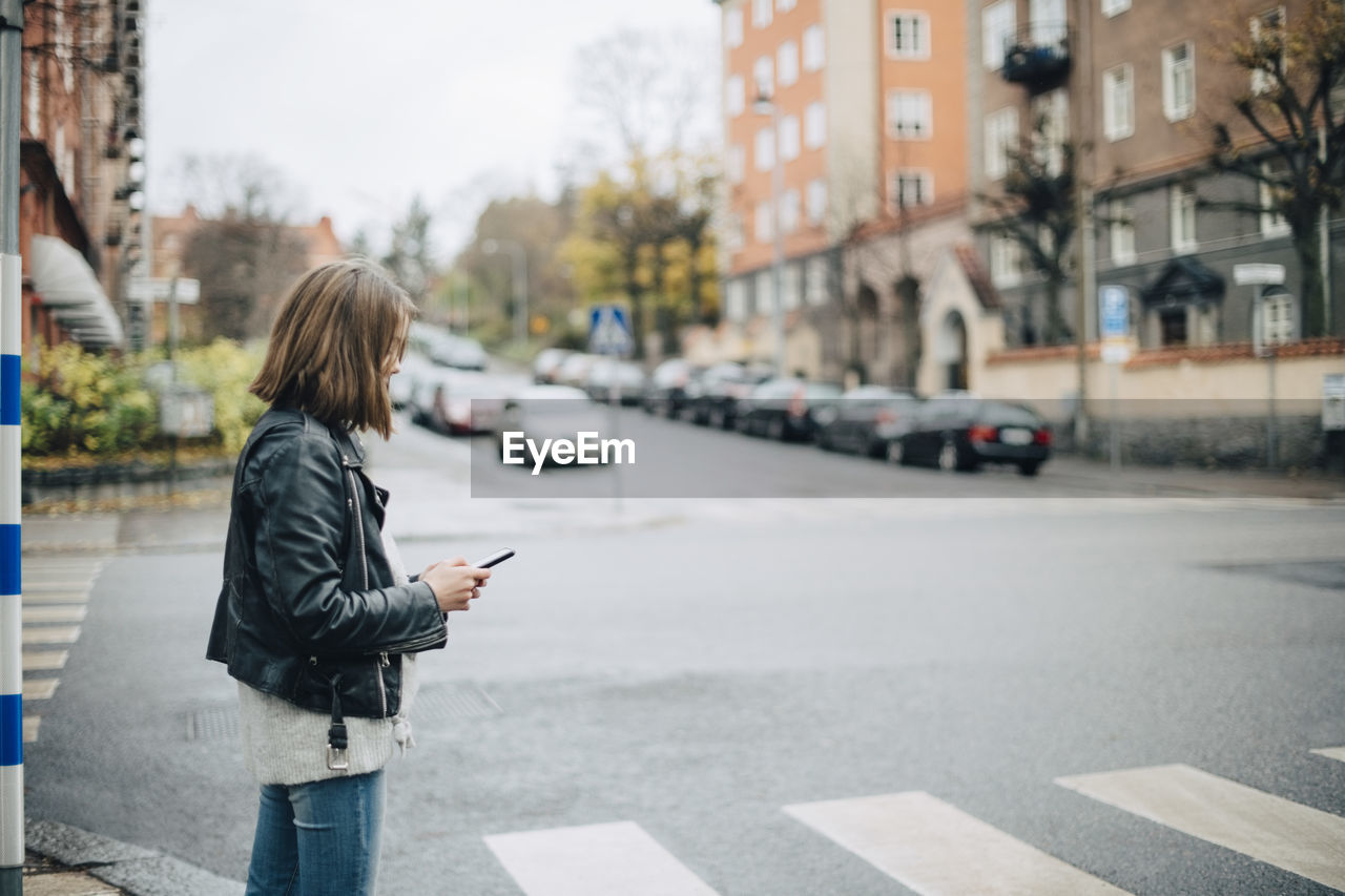 Side view of girl using mobile phone while standing on city street