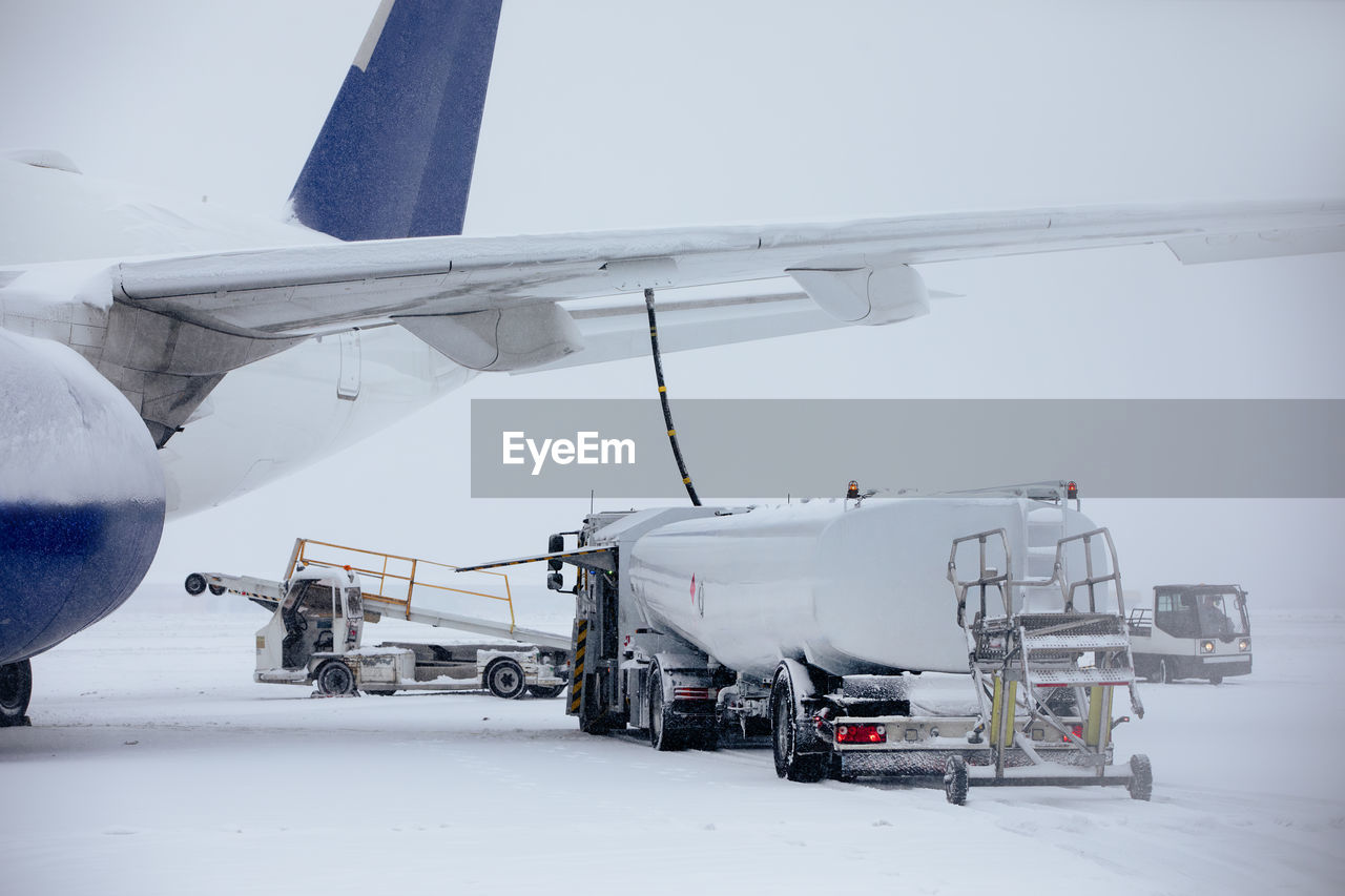 Refueling of airplane from fuel tanker at airport during snowfall. ground service on winter day.
