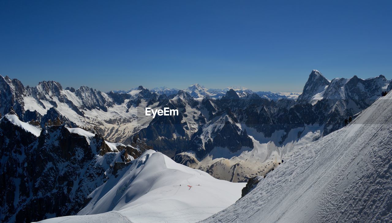 Scenic view of snowcapped mountains against clear blue sky, mountain climbers on the glacier
