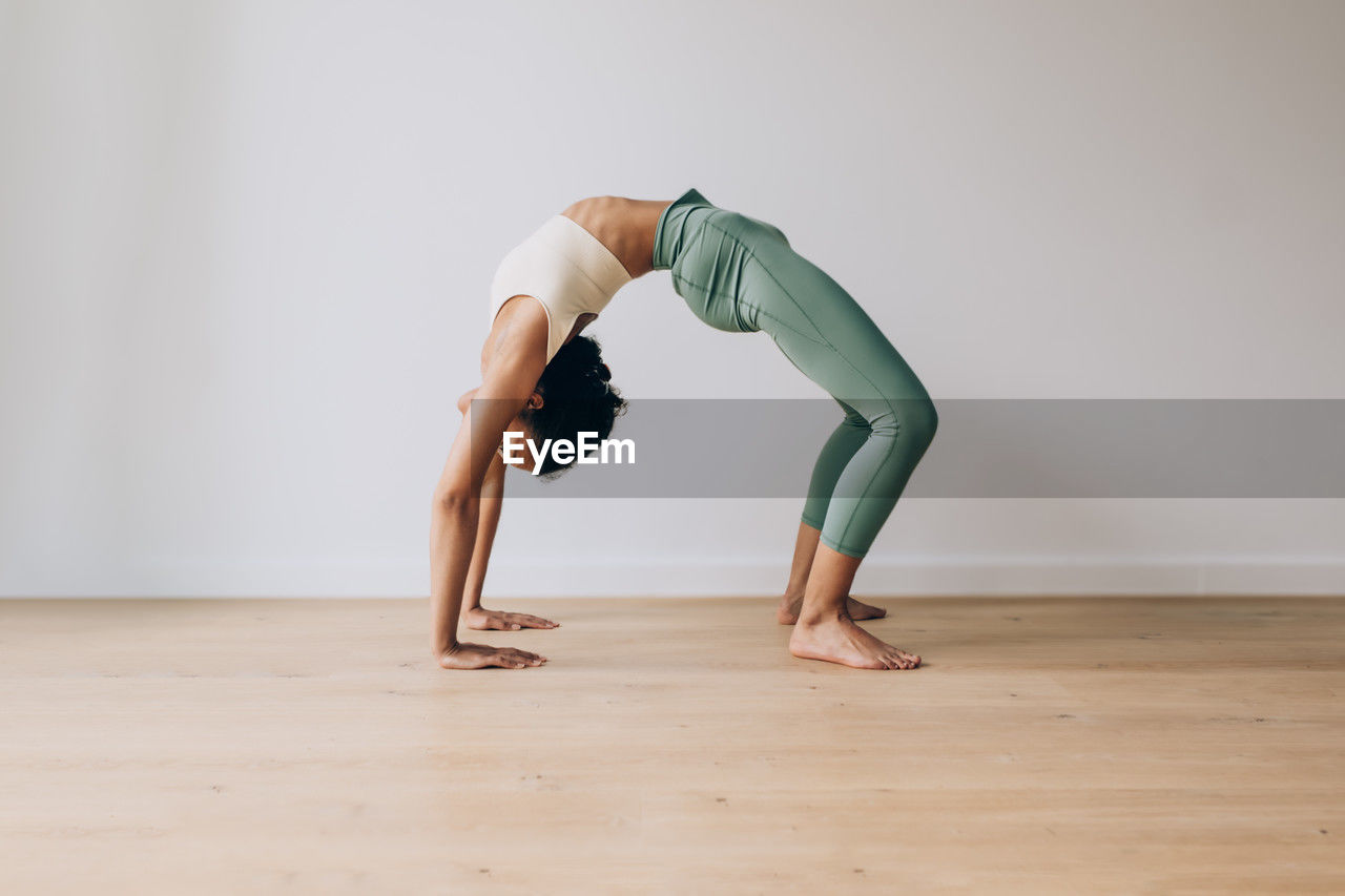 Yoga teacher practicing yoga position of bridge against white wall and wood floor with copy space