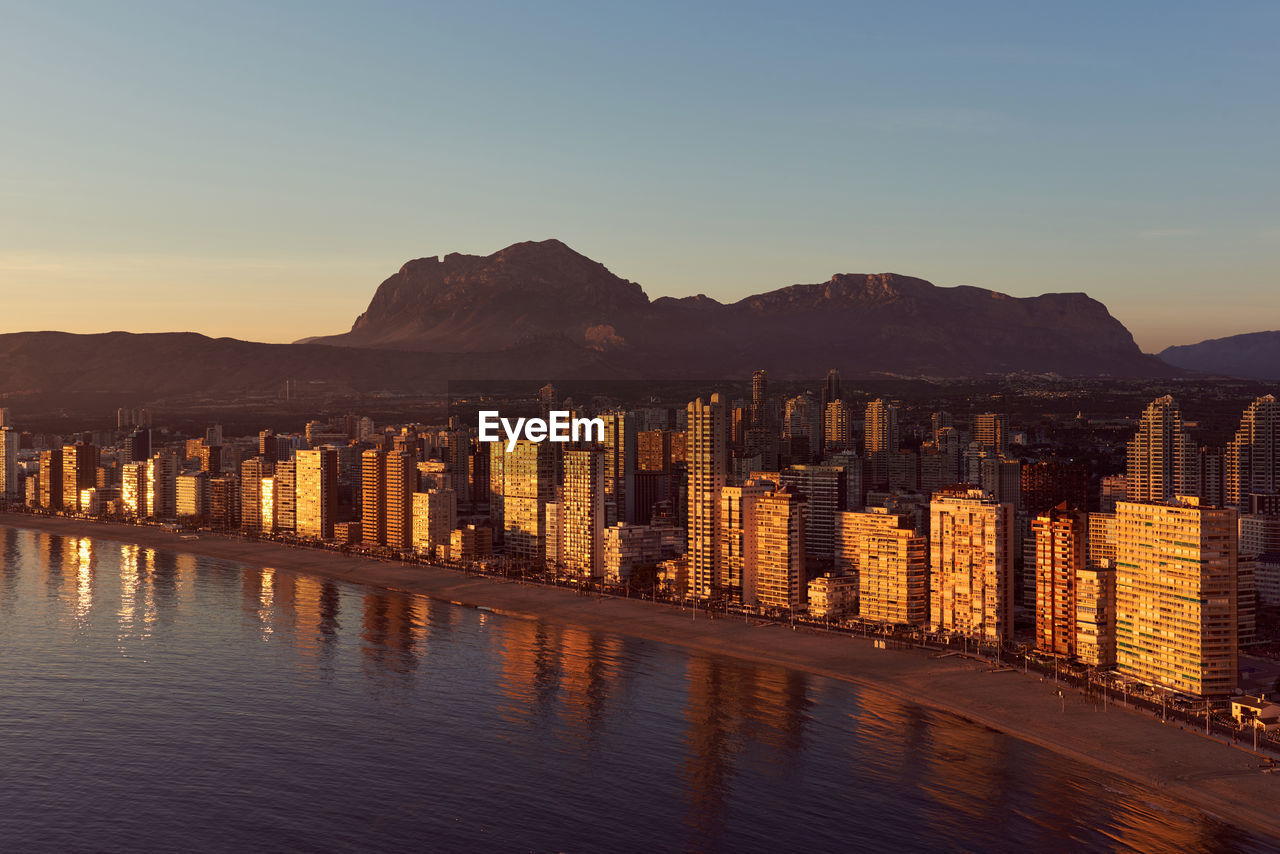 Aerial view of sea by city against sky at sunset